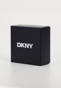 Scatola rettangolare nera con una texture opaca e liscia, caratterizzata da un prominente logo bianco "DKNY" sulla parte frontale.