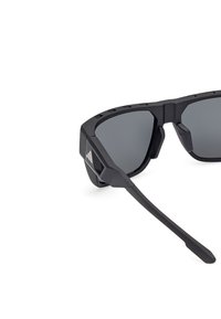 Ochelari de soare sport cu ramă neagră mată, design unghiular, lentile gri, accente texturate și un logo pe lateral.