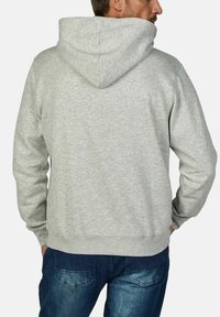 Lichtgrijze hoodie met een ruime capuchon, gemaakt van zacht materiaal, met een eenvoudig ontwerp en geribde manchetten, gedragen met blauwe jeans.