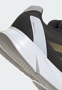 Černá atletická bota s prodyšným síťovaným svrškem a zlatými akcenty. Má bílou mezipodešev a texturovanou gumovou podešev pro lepší přilnavost.