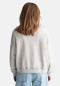 Sudadera gris con un corte holgado, hombros caídos y puños acanalados. Combinada con denim azul claro, mostrando un estilo casual.