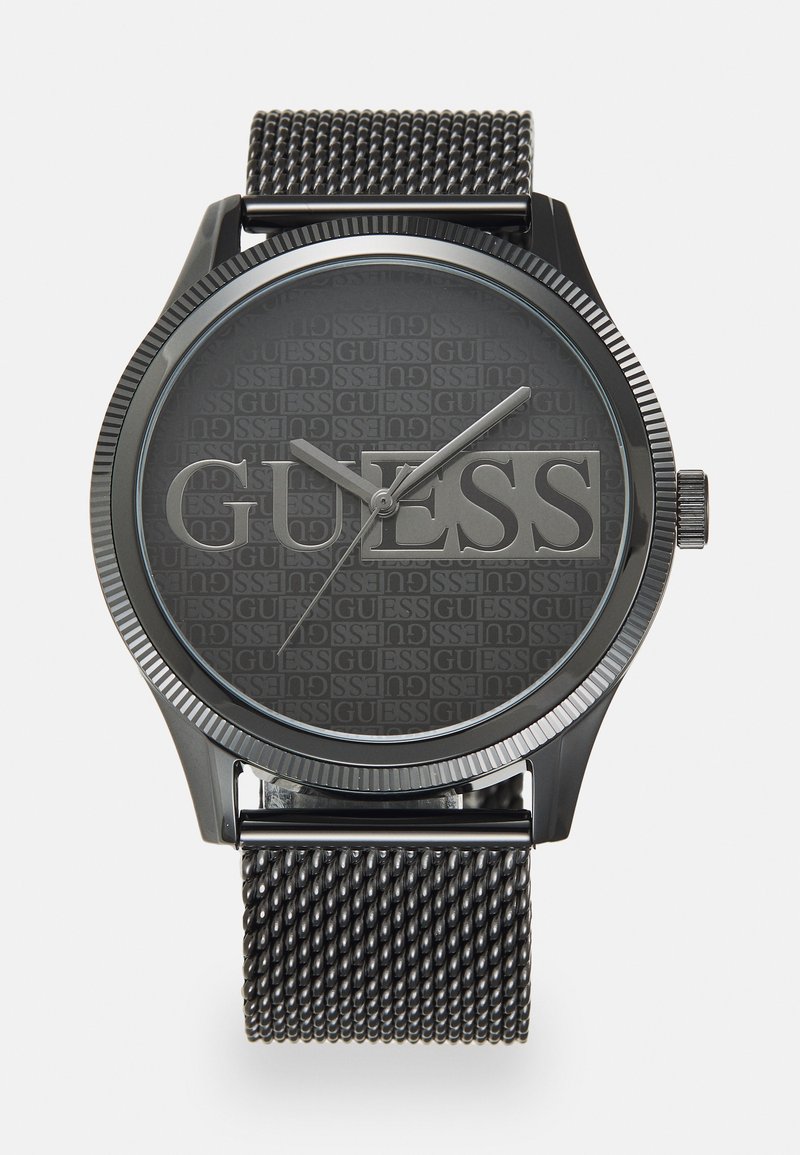 Black watch with a textured dark gray dial featuring the brand name "GUESS." It has a mesh stainless steel strap and silver hour markers.