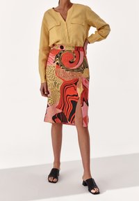 Camisa de lino amarilla con dos bolsillos en el pecho, combinada con una falda lápiz de patrón colorido que presenta diseños abstractos en rojo, rosa y negro.