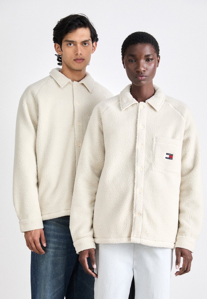 Fleece button-up jassen in crèmekleur, met een kraag, een voorkantzak en geribde manchetten. Modellen dragen ze met denim onderkleding.