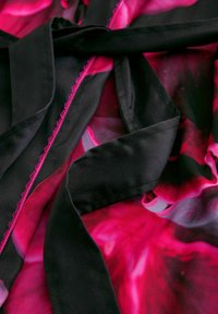 Mustalla ja vaaleanpunaisella kuviolla varustettu kangas, jossa on sileä pinta. Esittelee kukkasuunnittelua eloisassa vaaleanpunaisessa mustaa taustaa vasten, ja näkyvät ompeleet.