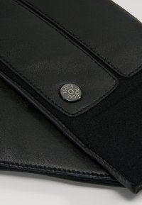 Portafoglio in pelle nera con finitura texturizzata, dotato di un bottone a pressione metallico etichettato "TOUCH" e foderato in tessuto liscio.
