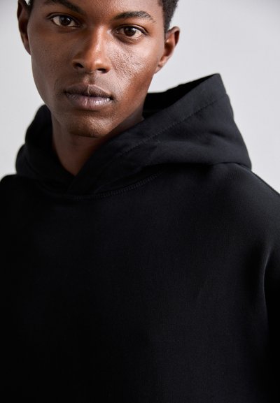 Sweatshirt à capuche noir en mélange de coton, avec une grande poche avant, une capuche avec cordon de serrage réglable et des poignets côtelés. Texture lisse.