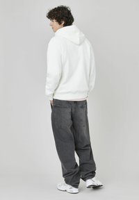 Sweat-shirt à capuche blanc, pantalon large gris foncé et baskets blanches. La tenue présente une coupe décontractée et un tissu doux, avec des coutures visibles et des poches.