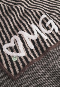 Tissu rayé noir et beige présentant un design en peluche blanc "OMG" et un cœur, avec une bordure cousue marron et un petit détail d'accent vert.