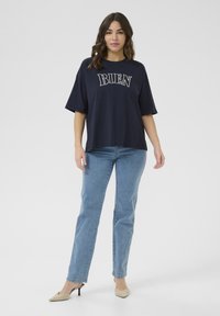 T-shirt en coton oversize bleu marine avec l'inscription blanche "BIEN", assorti à un jean droit bleu clair et des mules à talons beiges.