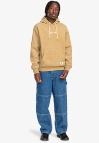 Khaki corduroy hoodie with a front pocket and "ONLY YOU" text. Paired with loose, blue denim pants featuring visible seam details. Black shoes.