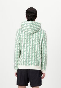 Felpa con cappuccio bianca con un motivo geometrico verde. Presenta polsini e orlo a costine, con un design in tessuto testurizzato.