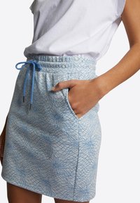 Světle modrá sukna s potiskem, pružným pasem se stahovací šňůrkou a bočními kapsami, se geometrickým, strukturovaným vzorem na bílém pozadí.