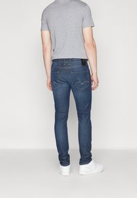 Jeans verdes ajustados de mezclilla con un acabado deslavado, cinco bolsillos y una etiqueta de cuero negra en la cintura, combinados con una camiseta gris.