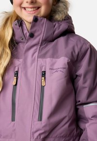 Lila wasserdichte Jacke mit einer mit Fell gefütterten Kapuze, zwei Reißverschlusstaschen und Logodetails. Verfügt über graue Akzente und eine glatte Textur.