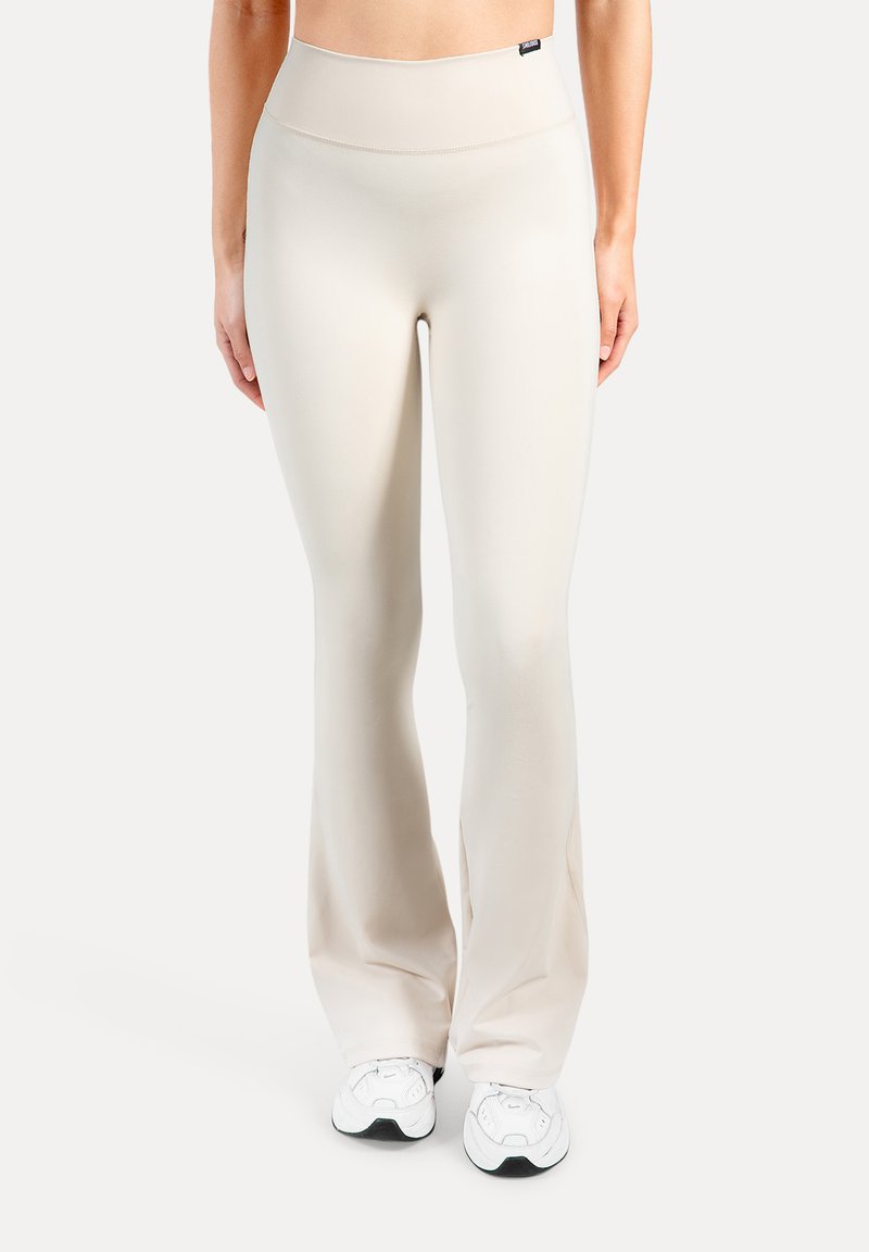 Beige, hoog getailleerde flared legging gemaakt van een gladde, rekbare stof. Voorzien van een brede tailleband en subtiele naden. Combineert goed met witte sneakers.