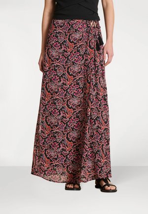 Femme portant un haut noir et une longue jupe portefeuille fluide avec un motif floral cachemire rouge et rose, assortie à des sandales noires.