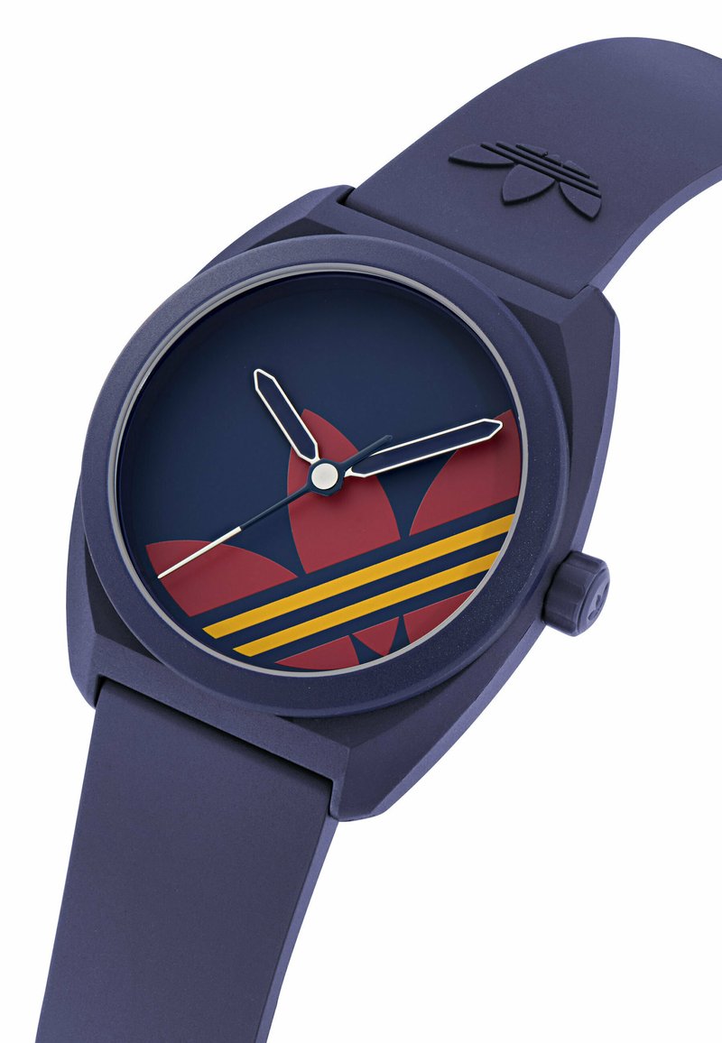 Montre-bracelet bleu marine avec logo trefoil Adidas rouge et rayures jaunes sur le cadran, aiguilles des heures et des minutes argentées, et bracelet en silicone bleu.