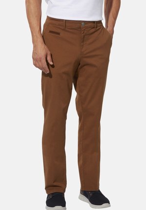 Man wearing brown straight-leg pants with side and chest pockets, paired with black sneakers and a white shirt.