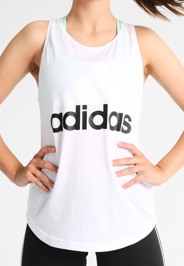 Débardeur blanc sans manches avec un grand logo "adidas" noir, en tissu doux et coupe décontractée, associé à un legging de sport noir.