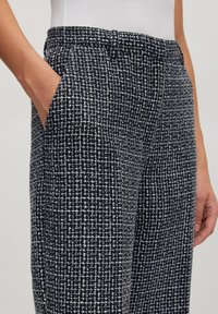 Textuur navy broek met een wit rasterpatroon, zijzakken en een soepele tailleband. De stof heeft een geweven uitstraling met subtiele diepte.
