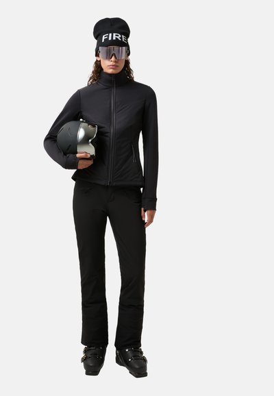Czarna kurtka narciarska z zamkiem z przodu, w połączeniu z czarnymi spodniami narciarskimi. Model nosi czarną czapkę z napisem "FIRE", lustrzane okulary przeciwsłoneczne i trzyma kask.