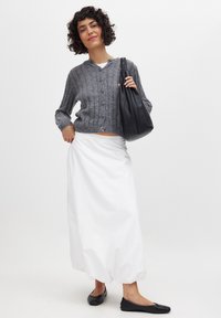 Cardigan grigio lavorato a maglia con collo rotondo e bottoni, abbinato a una gonna bianca fluida e scarpe nere basse. Include una borsa a spalla nera.