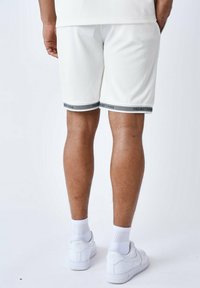 Pantalones cortos deportivos blancos con una textura acanalada, con una cinturilla gris etiquetada como "PROJECT X PARIS." Combinados con zapatillas blancas y calcetines de caña corta.