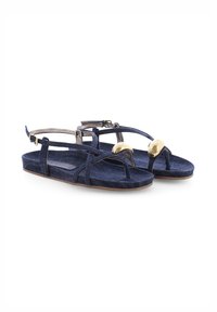 Denim sandalen in een donkerblauwe kleur, met gekruiste banden, een platte zool en gouden accenten bij de teen en enkel.