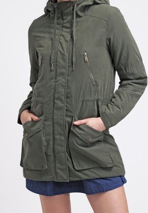 Veste à capuche vert olive avec fermeture éclair à l'avant, deux poches poitrine, taille élastique et cordons de serrage ajustables. Texture de tissu lisse.