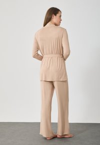 Μπεζ σετ loungewear που περιλαμβάνει ένα μπλουζάκι με μακριά μανίκια και ζωνάκι στη μέση, καθώς και παντελόνι φαρδύς γραμμής. Μάλακο και απαλό ύφασμα με άνετη εφαρμογή και χωρίς σχέδια.