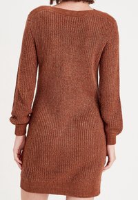 Robe pull tricotée couleur rouille avec des manches longues. Tissu texturé, poignets et ourlet côtelés, et un design à coupe relaxée.