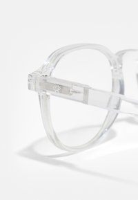 Ochelari de vedere din plastic transparent cu un cadru rectangular, având margini ușor rotunjite și o textură netedă. Branding notabil pe braț.
