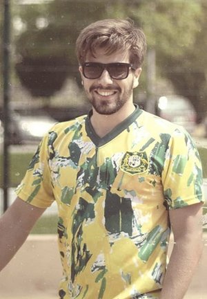 Geel en groen voetbalshirt met korte mouwen, voorzien van abstracte patronen en een v-hals. Bevat een logo op de linkerkant van de borst. Zonnebril gedragen.