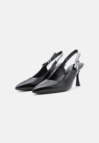 Tacones slingback de charol negro con punta afilada, correas estrechas que presentan una marca blanca y un diseño de tacón de aguja.