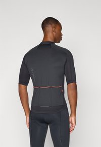 Maglia da ciclismo aderente a maniche corte nera, con tessuto testurizzato e un accento arancione in vita, dotata di dettagli riflettenti.