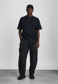 Czarny t-shirt z krótkim rękawem o kontrastowych szwach, w połączeniu z luźnymi czarnymi spodniami i czarnymi trampkami. Czapka dopełnia monochromatyczny wygląd.