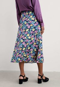 Floral midi skirt featuring a navy background with multicolored tulip patterns, a side slit, and a matching purple blouse. Black heeled sandals.