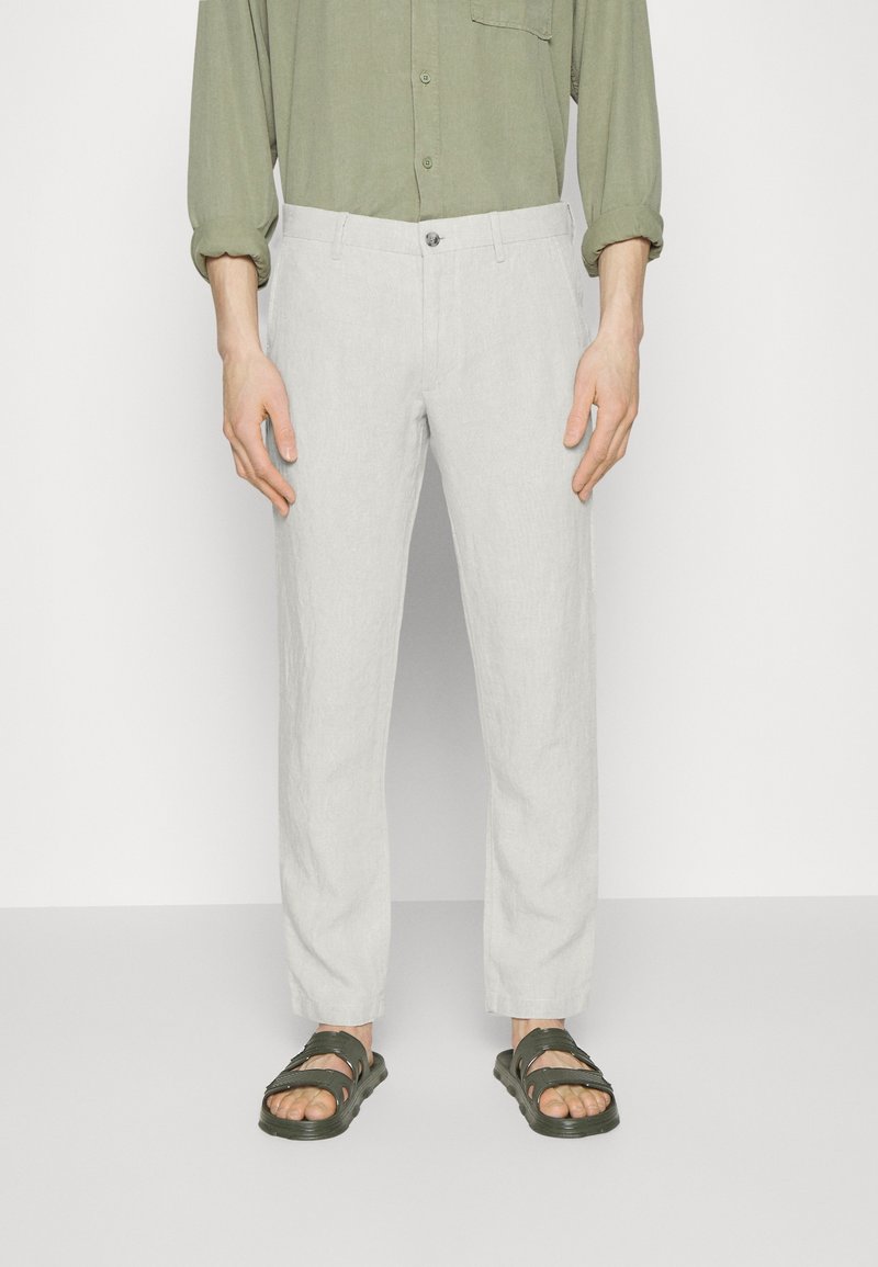 Hellgraue Leinenhose mit lockerem Sitz und geradem Bein, ausgestattet mit einem einzelnen Knopfverschluss vorne und Taschen. Kombiniert mit dunklen Sandalen.