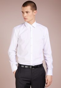 Camisa de vestir de manga larga blanca con cuello abotonado, corte ajustado, textura suave, combinada con pantalones oscuros y un cinturón negro.