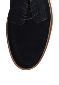 Zamszowe granatowe buty z okrągłym noskiem, brązową gumową podeszwą oraz kontrastowym detalem w sznurowaniu. Posiada przeszycia wzdłuż górnej krawędzi.