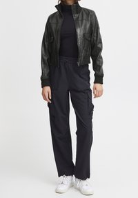 Černá kožená zkrácená bunda s žebrovanými manžetami, kombinovaná s námořnicky modrými cargo kalhotami a bílými teniskami. Oblečení má vysoký límec a kapsy.