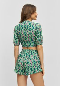 Top corto a maniche corte con motivo floreale verde, abbinato a pantaloni shorts con elastico in vita; entrambi presentano un design ondulato e dettagli con orlo arricciato.