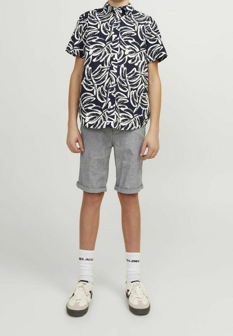 Camicetta a maniche corte con motivo di foglie in bianco e nero, abbinata a pantaloni corti grigi con risvolto e calze bianche, completata da sneakers.