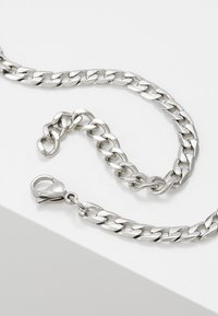 Hopeaketju, joka sisältää toisiinsa kytkeytyviä litteitä linkkejä, kiiltävän pinnan ja lukkoklipin turvallista kiinnitystä varten.