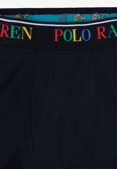 Črne kratke hlače z barvnim pasom, na katerem je v poudarjenih črkah napis "POLO RALPH LAUREN". Mehka tkanina, elastičen pas in gladka tekstura.