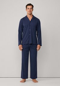 Juego de pijama azul marino en tela suave, con un diseño estampado y acentos en azul claro. La parte superior tiene un cierre de botones y cuello, y los pantalones son de pierna recta.