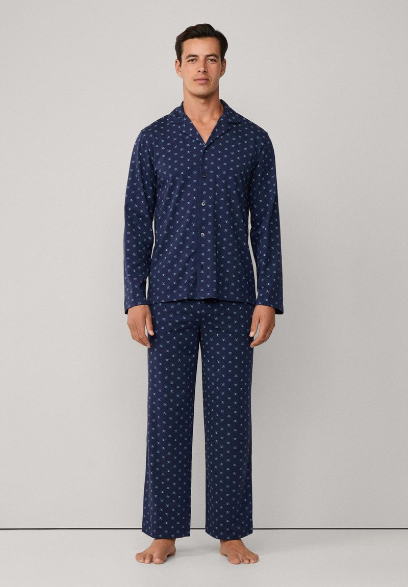 Juego de pijama azul marino en tela suave, con un diseño estampado y acentos en azul claro. La parte superior tiene un cierre de botones y cuello, y los pantalones son de pierna recta.
