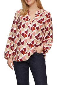 Lange mouwen blouse van lichte stof met een geometrisch patroon van bordeauxrood, roze en beige cirkels. Gekleurde kraag en geplooide manchetten.