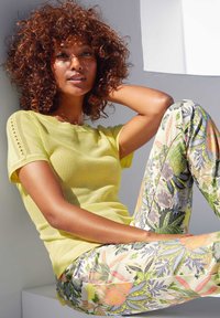 Geel net gebreide top in combinatie met bloemenpatroon broek met levendige bladeren en bloemen in tinten groen, roze en blauw.